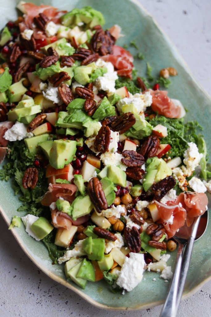 Farverig vinter­salat med grønkål, parmaskinke og karamelliserede paranødder serveret på fad.