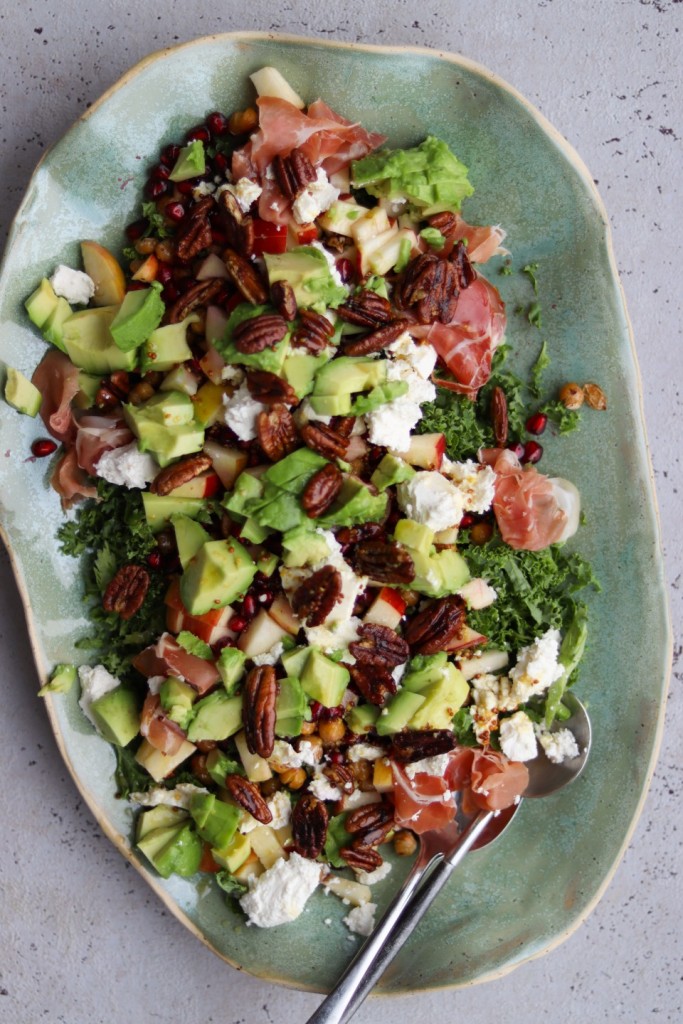 Farverig vinter­salat med grønkål, parmaskinke og karamelliserede paranødder serveret på fad.